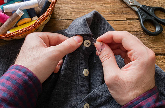 Kleren repareren: man naait knoop van zijn overhemd er weer aan.