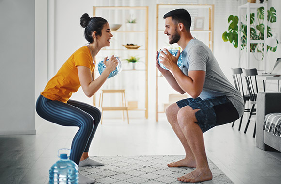 Twee sporters gebruiken waterflessen als gewichten tijdens een full-body workout thuis.