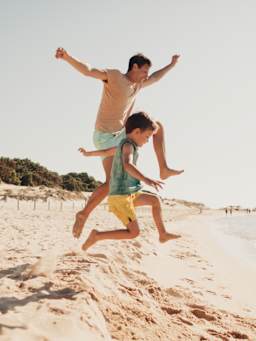 Dove andare in vacanza con i bambini: un papà e un bambino saltano sulla sabbia in Sardegna.