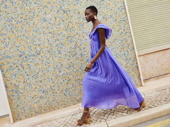Vrouw in lange, paarse A-lijnjurk loopt op hoge hakken over straat | C&A