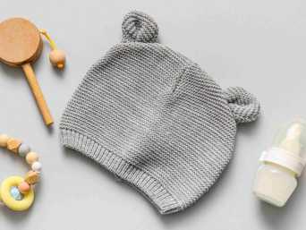 Graue Babymütze mit Öhrchen zwischen Flasche und Spielzeug Graue Babymütze mit Öhrchen zwischen Flasche und Spielzeug