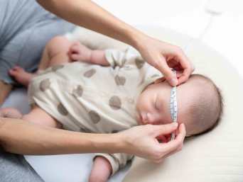 Frau misst mit einem weichen Maßband den Kopfumfang eines Babys für seine Mützengröße. Frau misst mit einem weichen Maßband den Kopfumfang eines Babys für seine Mützengröße.