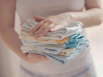 Frau hält Stapel mit sauberer Babykleidung als Symbolbild für die Frage "Wie viel Kleidung braucht ein Baby?" Frau hält Stapel mit sauberer Babykleidung als Symbolbild für die Frage "Wie viel Kleidung braucht ein Baby?"
