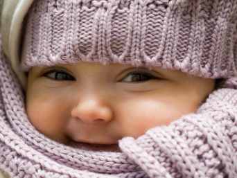 Close-up von glücklichem Baby in dicker Winterkleidung mit Schal und Mütze.