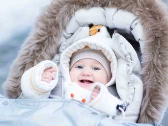 Lachendes, dick angezogenes Winterbaby im Kinderwagen.