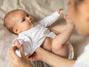 Frau zieht einem Baby einen weißen Body an Frau zieht einem Baby einen weißen Body an