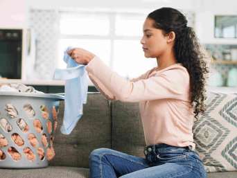Frau kontrolliert nach dem Waschen, ob alle Flecken aus einem blauen Babystrampler entfernt wurden. Frau kontrolliert nach dem Waschen, ob alle Flecken aus einem blauen Babystrampler entfernt wurden.