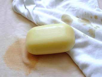 Ein Stück Gallseife auf beigem und weißem Stoff mit Flecken Ein Stück Gallseife auf beigem und weißem Stoff mit Flecken