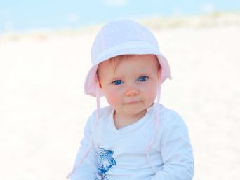 Baby in Sommerkleidung (Sonnenhut und lange Ärmel) am Strand im Schatten. Baby in Sommerkleidung (Sonnenhut und lange Ärmel) am Strand im Schatten.