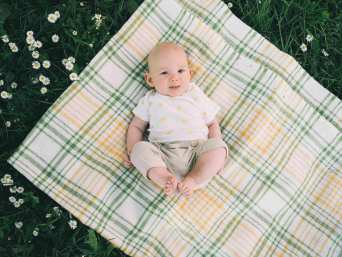 Baby in Sommerkleidung liegt auf einer karierten Picknickdecke im grünen Gras. Baby in Sommerkleidung liegt auf einer karierten Picknickdecke im grünen Gras.