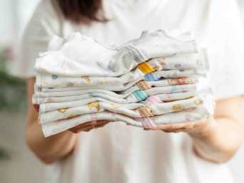 Frau in weißem T-Shirt hält einen Stapel Babysachen, die gewaschen und gefaltet wurden. Frau in weißem T-Shirt hält einen Stapel Babysachen, die gewaschen und gefaltet wurden.