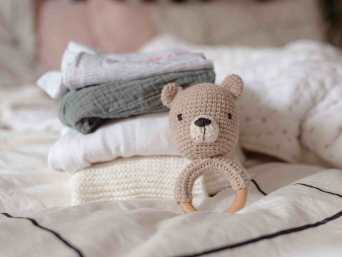 Ein Stapel Babykleidung und ein Spielzeug auf einem Bett. Ein Stapel Babykleidung und ein Spielzeug auf einem Bett.