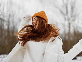 Glückliche Frau mit gelber Mütze und weißem Pullover im Winter.