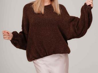 Blonde Frau in weißem Seidenkleid, das mit einem braunem Pullover wintertauglich kombiniert wurde.