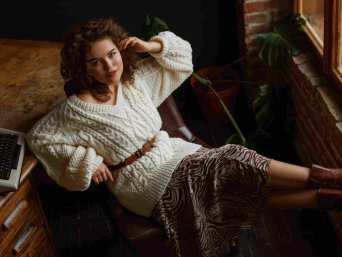 Bild von sitzender, gut gekleideter Frau in weißem Pullover zeigt, dass man ein Kleid mit Pulli kombinieren kann.