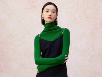 Stylische Frau mit grünem Rollkragen-Pulli unter schwarzem Trägerkleid.