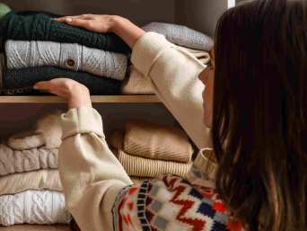 Frau mit braunem Haar räumt Strickpullover in ihren Kleiderschrank ein.
