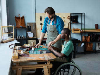 Ausbildung mit körperlicher Behinderung – Azubi im Rollstuhl arbeitet in einer Lederwerkstatt. 