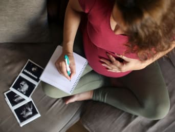 Schwangere Frau schreibt Namensideen für ihr Baby in ein Notizbuch.