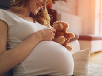 Zwangere vrouw houdt een teddybeer tegen haar babybuik.