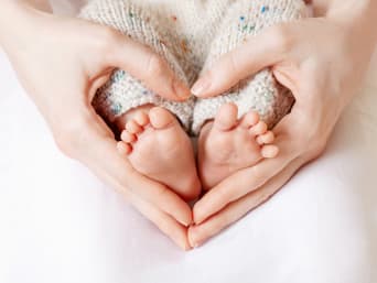 Des mains entourent les pieds d’un bébé et forment un coeur.