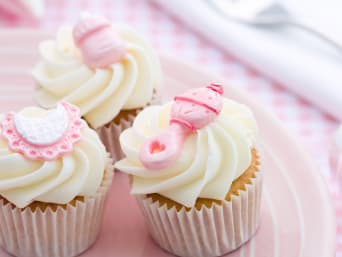 Des cupcakes blancs avec une décoration rose pour une baby shower.
