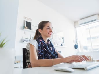 Une femme assise de façon ergonomique à son bureau au travail pour éviter d’avoir mal au dos.