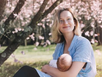 Reggiseni per l’allattamento per un maggiore confort e sostegno: una donna allatta il suo bebè in un parco.