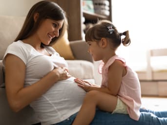 Biustonosz ciążowy dla większej wygody podczas oczekiwania na dziecko: ciężarna mama bawi się z córeczką.