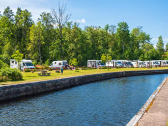 Wohnmobile stehen auf einem Campingplatz in der Nähe eines Kanals.