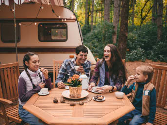 Przyczepa campingowa – rodzina je podwieczorek na polu kempingowym.