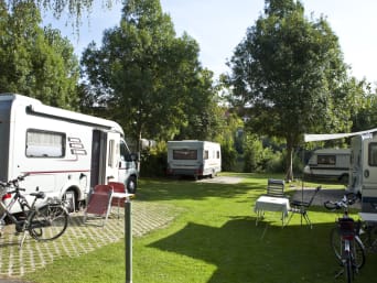 Camping Knigge: Blick auf geparkte Wohnmobile mit Campingmöbeln und Fahrrädern.