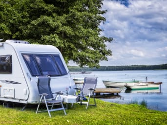 Campingregels: caravan staat met campingmeubels aan een meer.