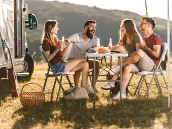 Camperplaats vinden – een groep vrienden is gezellig aan het borrelen voor hun camper.