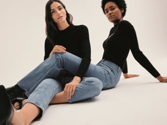 Ženy sedící na podlaze v džínách a černých topech.