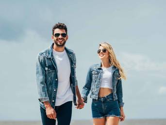 Jeansjacken kombinieren: Ein Pärchen in Jeansjacken hält Händchen.