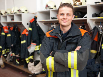 Vrijwillige brandweer: brandweerman staat in de kleedkamer met werkkleding aan.