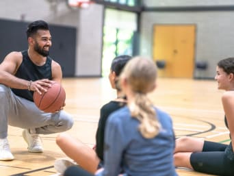 Wolontariat w szkole – trener tłumaczy dzieciom zasady gry w koszykówkę. 