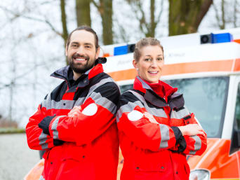 Voluntariado en emergencias: dos voluntarios con uniforme delante de una ambulancia.