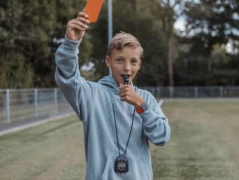 Bénévole en club de sport : un arbitre bénévole junior siffle lors d’un match.