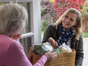Aiutare i vicini – Una vicina di casa porta la spesa a una signora anziana.