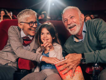 Wycieczka z dziadkami: dziadkowie i wnuczka oglądają film w kinie.