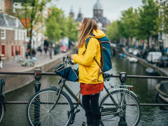 Jazda rowerem w deszczu: kobieta z rowerem w kurtce przeciwdeszczowej zwiedza miasto.