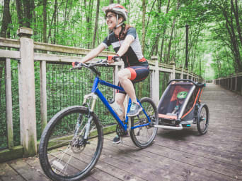 Una madre lleva a su hijo en un remolque de bicicleta a través de un parque urbano.