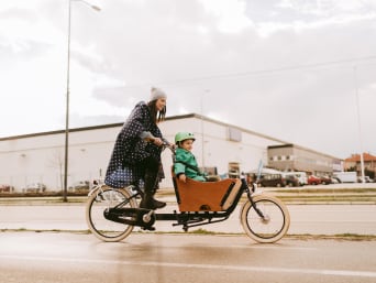 Cargo bike trasporto bambini: donna porta il suo bambino in bici con una cargo bike. 