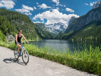Radtouren Oberösterreich: Frau fährt auf einem Radweg am See mit Blick auf Dachsteingletscher