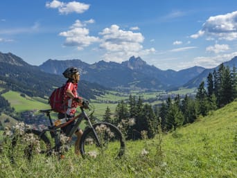 Radtouren Tirol: Eine Frau steht mit einem Fahrrad auf einer Wiese in Tirol.