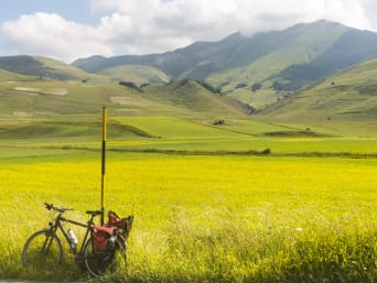 Piste ciclabili Umbria: foto di una bici e un panorama di collina nei pressi di Castelluccio di Norcia.