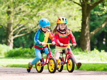 Zwei Kinder üben das Fahrradfahren zu Beginn mit einem Laufrad.