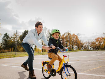 Fahrrad für Kinder: Vater übt das Radfahren mit seinem Kind auf einem Sportplatz.